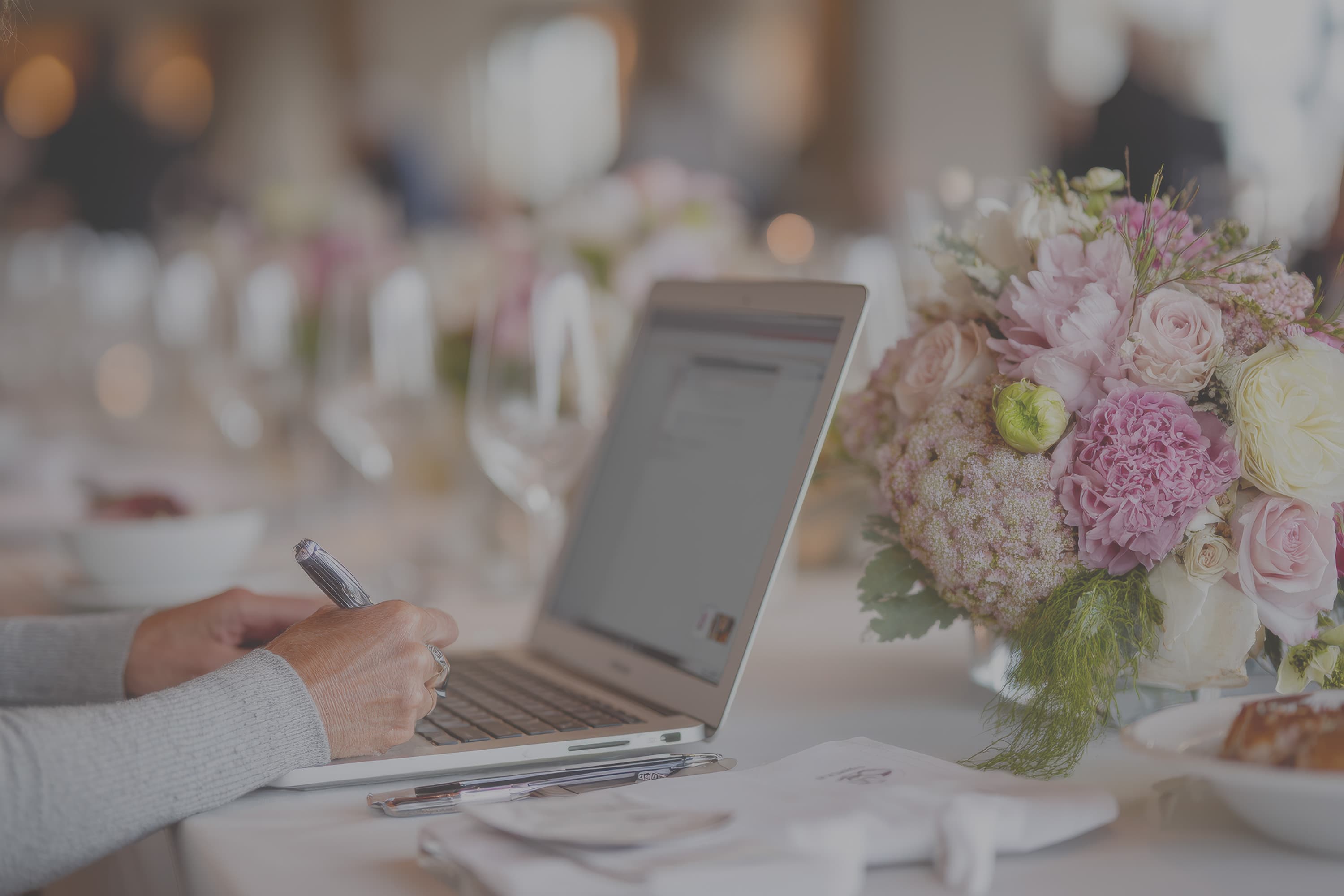 A wedding venue coordinator reviewing enquiry conversion figures on a laptop in a calm, sunlit venue office.