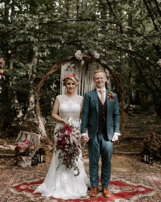 A couple standing hand in hand under a woodland ceremony arch at The Dreys